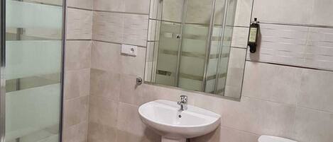 Un bany amb una cabina de dutxa de vidre, un lavabo de pedestal, un vàter i un mirall sobre el lavabo.