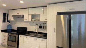 A modern kitchen with white cabinetry, stainless steel appliances, and a black countertop. - Penthouse Jacuzzi and Private Barbecue Exclusive (Santo Domingo)