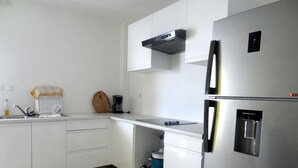 A modern kitchen with white cabinets, a stainless steel refrigerator, a coffee maker, and a microwave. - Waterfront T2 apartment (Les Trois-Îlets)