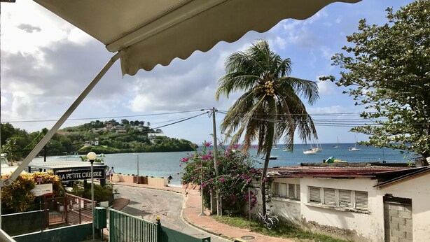 A coastal view with a palm tree, a sign reading "LA PETITE CREPERIE," and a view of boats on the water. - Waterfront T2 apartment (Les Trois-Îlets)