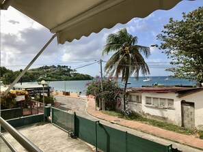 A coastal view with a palm tree, a sign reading "LA PETITE CREPERIE," and a view of boats on the water. - 2-Bedroom Apartment Near the Water (Les Trois-Îlets)
