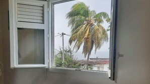 A room with a table and chairs, a window with a view of palm trees and buildings, and a white cabinet. - Waterfront T2 apartment (Les Trois-Îlets)