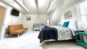 A bedroom with a bed, a sofa, a TV, and a window.