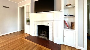 A living room with a fireplace, a flat-screen TV mounted above it, and built-in shelving with decorative items.