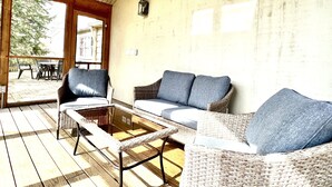 A covered patio area with wicker furniture, including a sofa and a chair, and a glass-top coffee table.