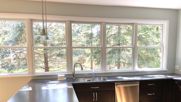 A modern kitchen with a large window, dark cabinetry, and a stainless steel dishwasher.