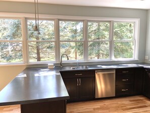 Una cocina moderna con un amplio ventanal, muebles oscuros y un lavavajillas de acero inoxidable.