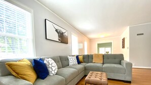 A modern living room with a grey sectional sofa, a small ottoman, and a framed picture on the wall.