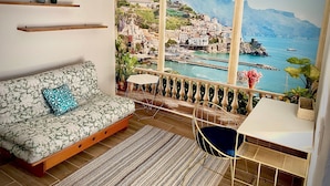 Ein Zimmer mit einer Couch, einem kleinen Tisch und Blick auf eine Küstenstadt durch ein großes Fenster.