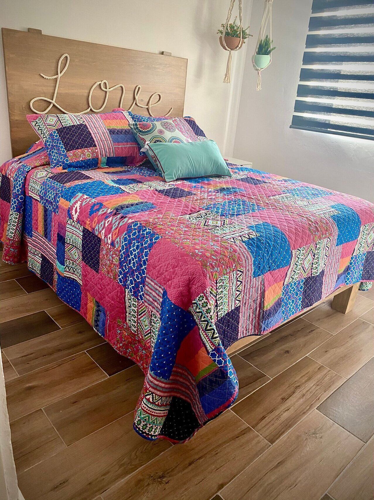 A bed with a colorful quilt, a wooden headboard with 'Love' written on it, and a hanging plant.