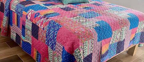 A bed with a colorful quilt, a wooden headboard with 'Love' written on it, and a hanging plant.