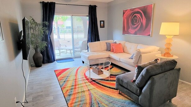 A living room with a white sofa, a grey armchair, a glass coffee table, a colorful rug, a large painting, and a lamp. - Ar`s Downtown R&R X2 A106 (Phoenix)