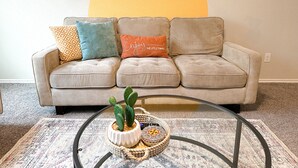 A beige sofa with three cushions, a glass coffee table, and a small potted plant.