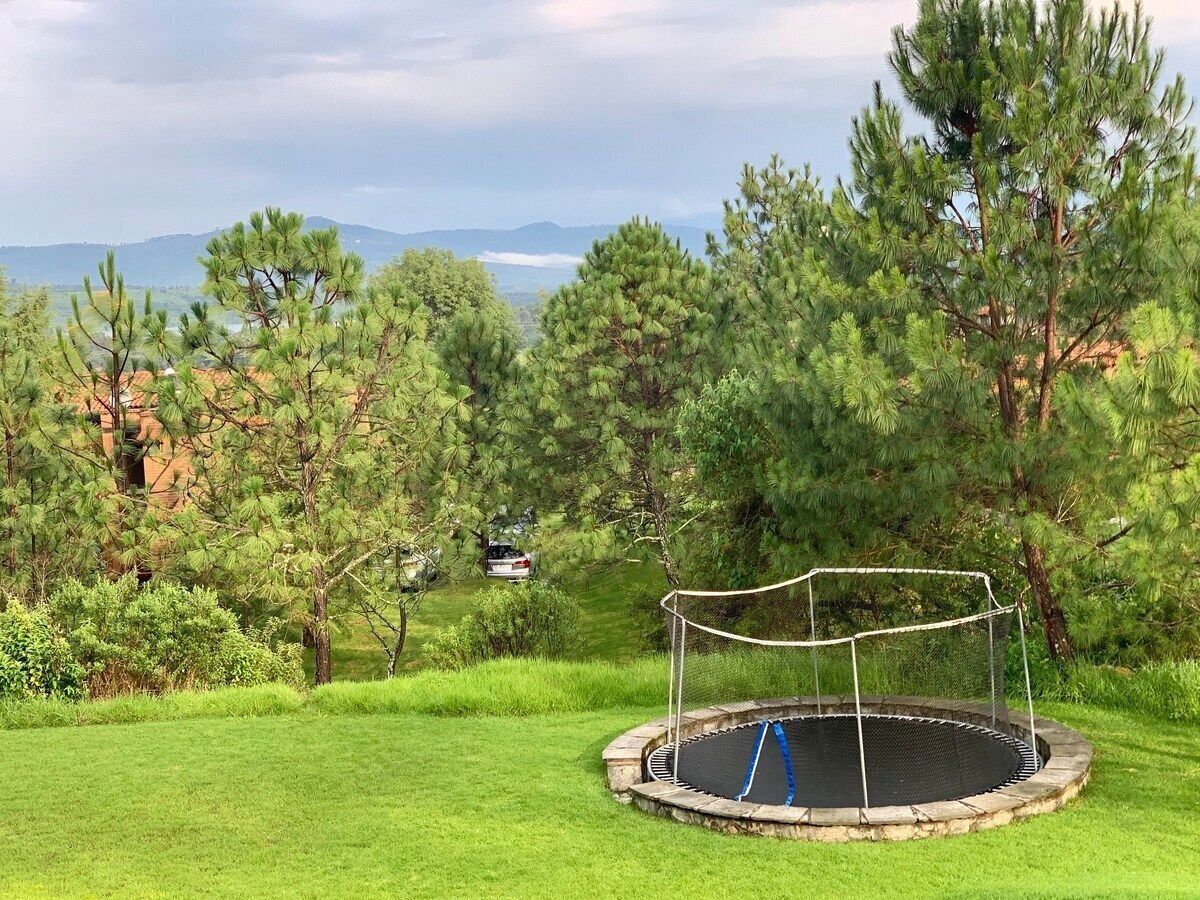 A trampoline in a grassy area with trees and a distant view of mountains.