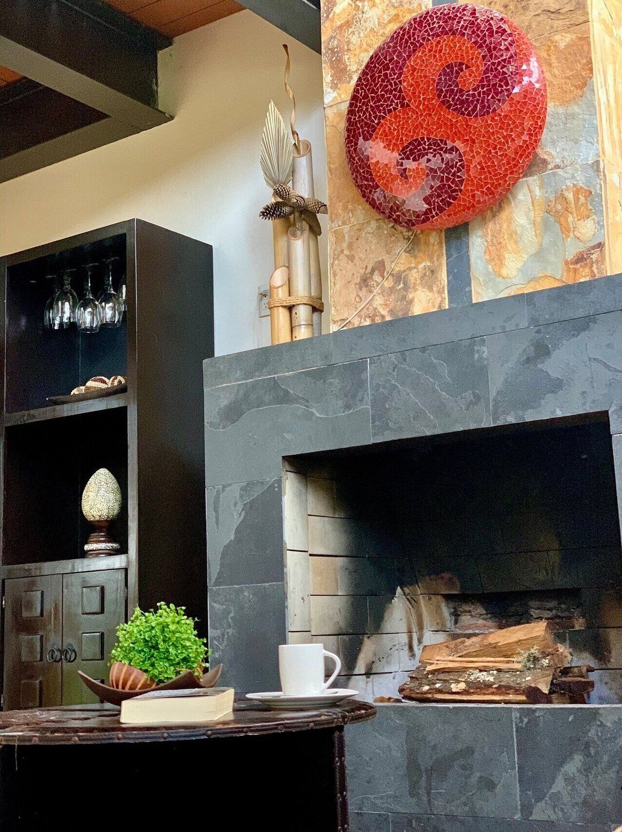 A modern interior with a fireplace, a decorative wall piece, and a shelf with glassware and a plant.