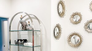 Une salle de bain dotée d’un meuble vitré où sont rangées les serviettes et les articles de toilette, d’une statue de paon décorative et de plusieurs miroirs en forme de soleil fixés au mur.