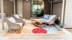 Un patio couvert aménagé avec des meubles en osier, une table en bois et un tapis aux couleurs vives.