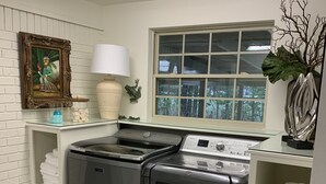 Une buanderie équipée d’un lave-linge et d’un sèche-linge à chargement frontal, d’une fenêtre donnant sur les arbres et d’une étagère où sont pliées les serviettes.