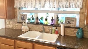A kitchen with a double sink, wooden cabinets, and a window with decorative plants. - Waterfront - Near Ark Encounter (Sparta)