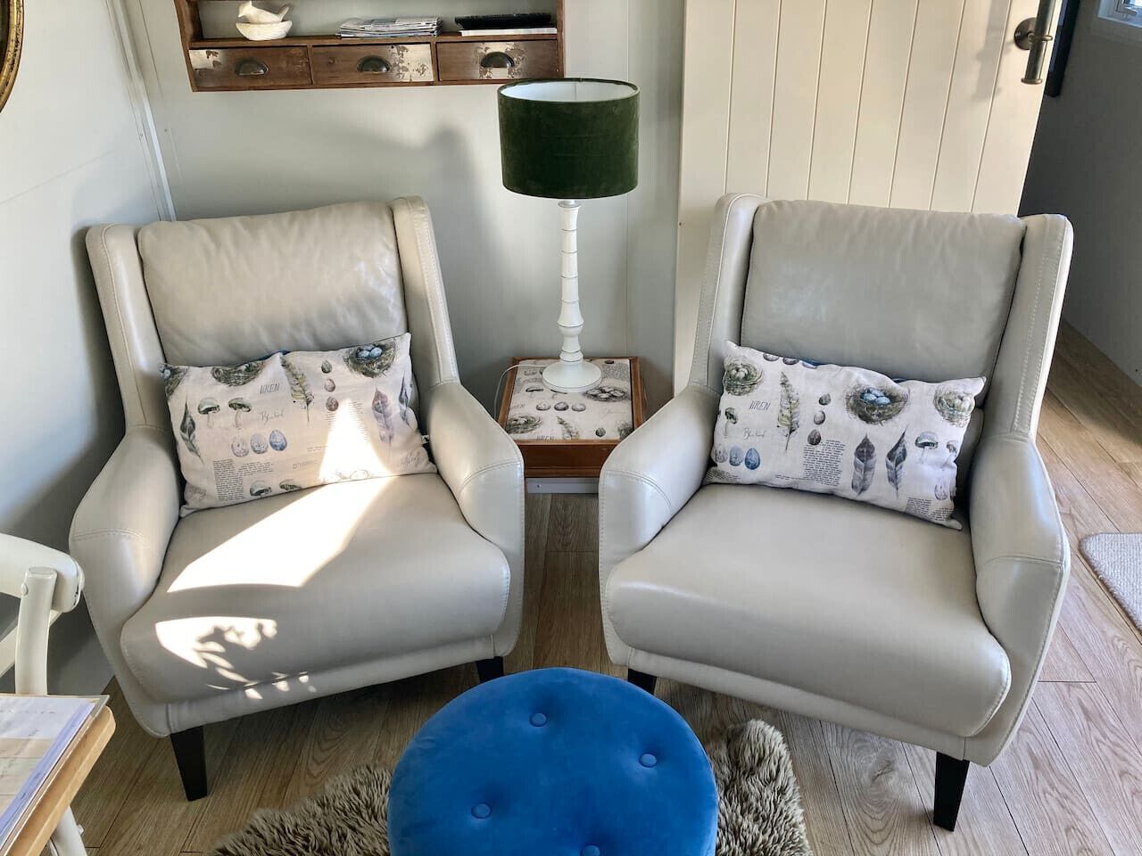 Deux fauteuils assortis avec des coussins identiques, une table d’appoint avec une lampe et un pouf bleu.