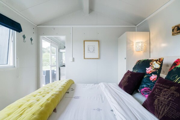 A room with a bed, a bench, a framed picture, and a wall-mounted light fixture.