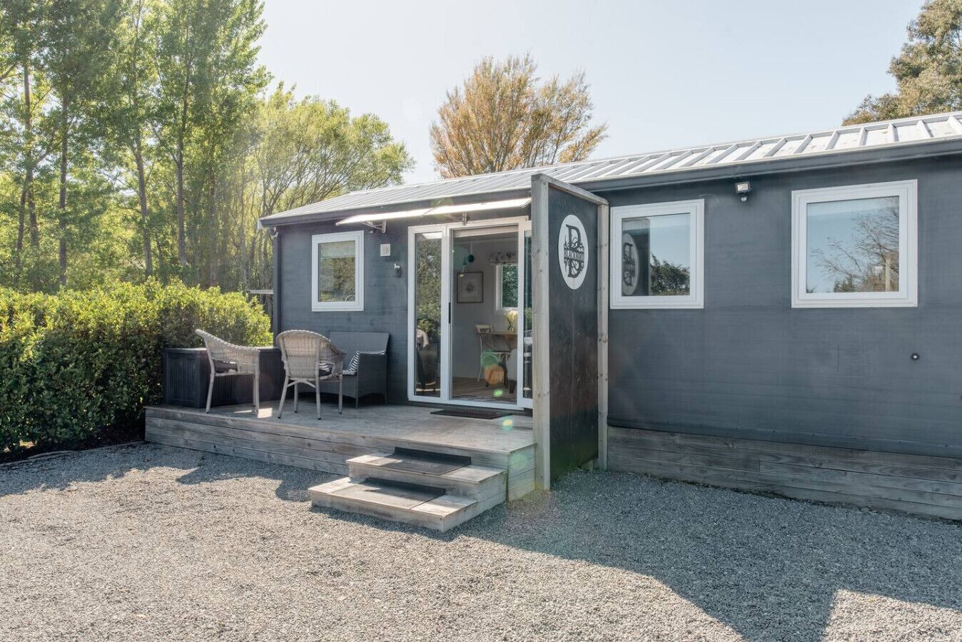 A compact, single-story building with a covered outdoor seating area, a small porch, and a gravel driveway.
