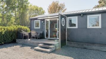 A compact, single-story building with a covered outdoor seating area, a small porch, and a gravel driveway.