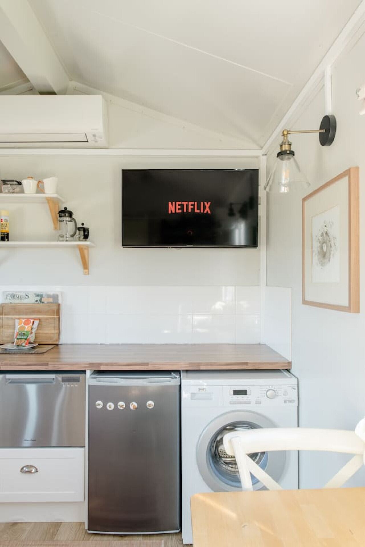 Une cuisine moderne équipée d’un lave-vaisselle encastré, d’un lave-linge et d’un téléviseur à écran plat fixé au-dessus du plan de travail, sur lequel est affiché le logo de Netflix.