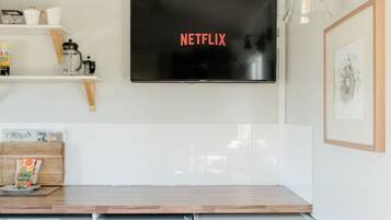Une cuisine moderne équipée d’un lave-vaisselle encastré, d’un lave-linge et d’un téléviseur à écran plat fixé au-dessus du plan de travail, sur lequel est affiché le logo de Netflix.