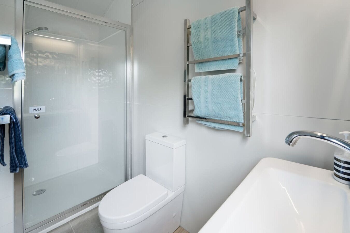 A bathroom with a glass-enclosed shower, a toilet, a towel rack with two towels, and a sink with a faucet.