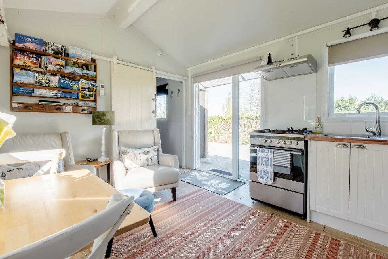 A modern kitchen with a gas stove, oven, and white cabinetry. There is a dining area with a table and chairs, and a bookshelf filled with books.