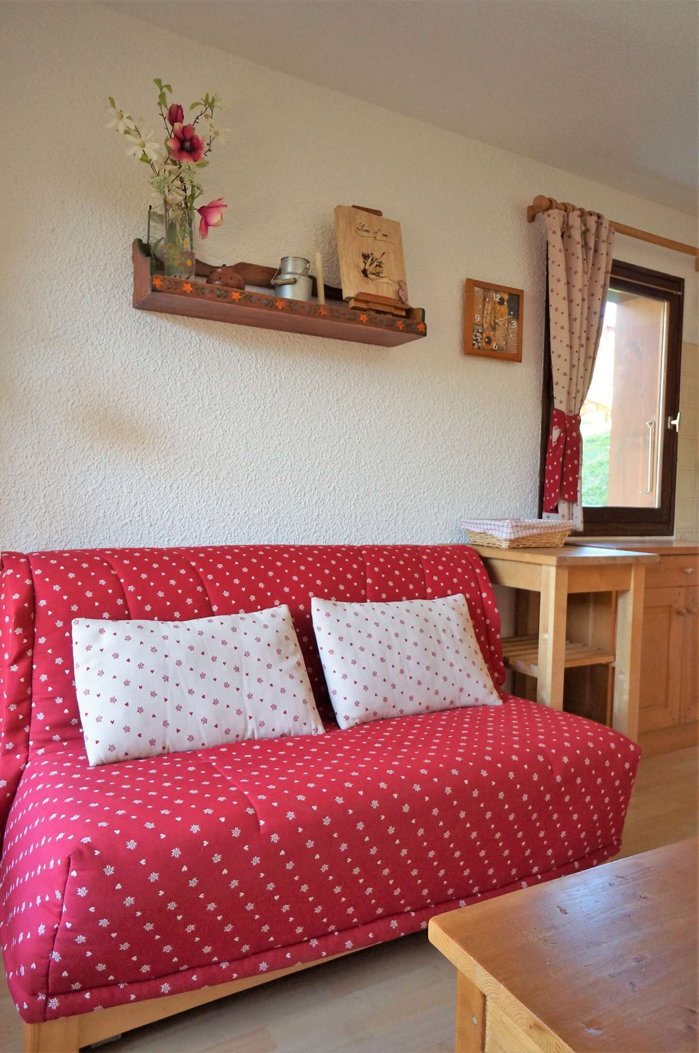 Ein rotes Sofa mit weißen Blumenmustern, ein Holztisch und ein Regal mit Dekorationen.