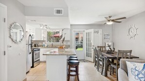 Una cocina moderna con armarios blancos, una isla central con taburetes y un comedor con mobiliario de madera.