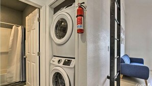 Una sala de bugaderia amb dues rentadores, un extintor, un sofà blau i una porta que dona a una altra habitació.