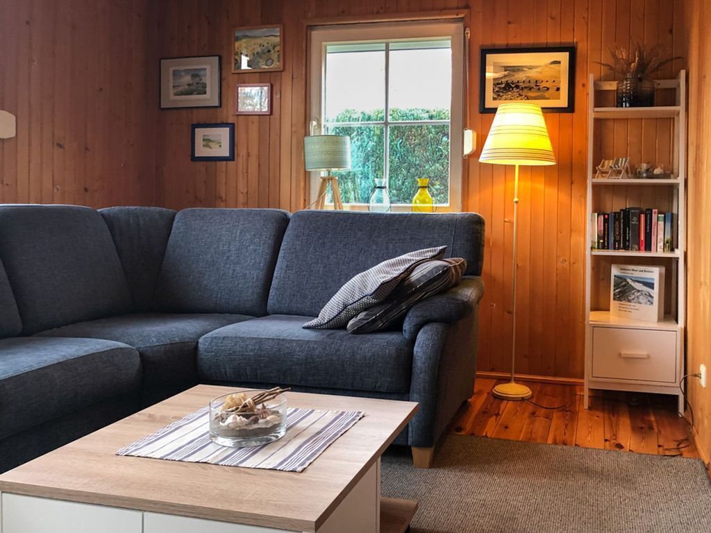 Ein gemütliches Wohnzimmer mit grauem Sofa, einem Holztisch und einem Bücherregal.