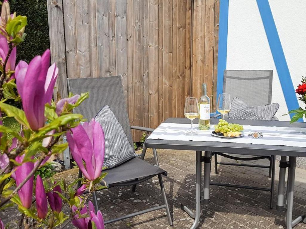 An outdoor dining area with a table set for two, featuring a white tablecloth, a bottle of white wine, and a plate of grapes.