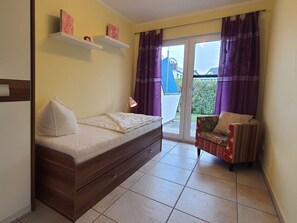 A small room with a bed, a chair, and a sliding glass door leading to an outdoor area.