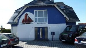Un edificio con un mural de un velero, una paleta de colores azul y blanco, una puerta y una ventana.