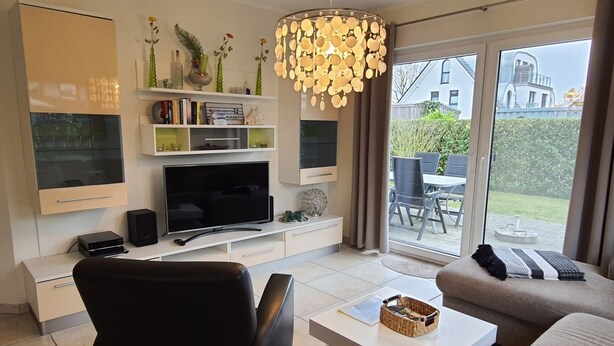 Una sala de estar moderna con un televisor de pantalla plana, un sillón de cuero negro, una mesa de centro blanca y un sofá beige.