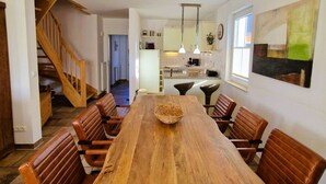 Un comedor amplio con una mesa de madera y sillas de cuero, una cocina al fondo y una escalera que sube a otro nivel.