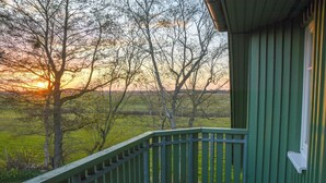 Een houten trap die leidt naar een groen gebouw met uitzicht op een zonsondergang boven een grasveld en bomen.