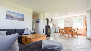 Een gezellige woonkamer met een bank, een houten salontafel en een open haard. Er is een eethoek met een tafel en stoelen.
