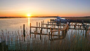 Een zonsondergang boven kalm water met een pier en een boot.