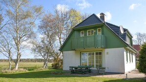 Een groen-wit huis met een balkon, een schotelantenne en een picknicktafel in de voortuin.