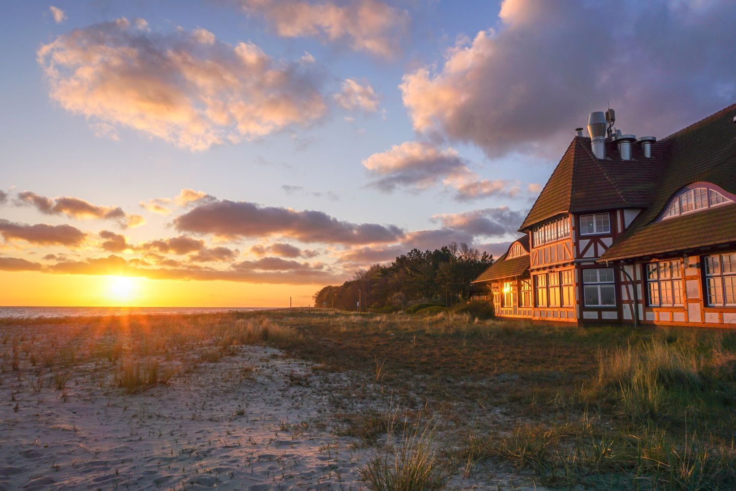 Ett traditionellt hus med korsvirkesfasad och sluttande tak, beläget på en sandstrand med havet som bakgrund.