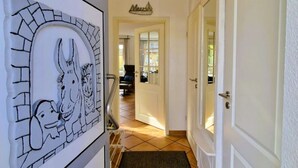 A hallway with a white door, a wall-mounted decorative panel, a tiled floor, and a ceiling light. - Mine Heimat 15 "Dat Röverhus" - bright, friendly semi-detached house (Zingst)