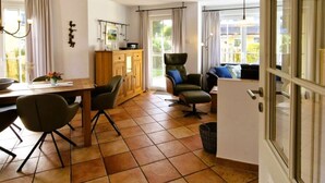 A spacious living area with a dining table, chairs, a sofa, and a chair. There is a cabinet and a window with curtains. - Mine Heimat 15 "Dat Röverhus" - bright, friendly semi-detached house (Zingst)