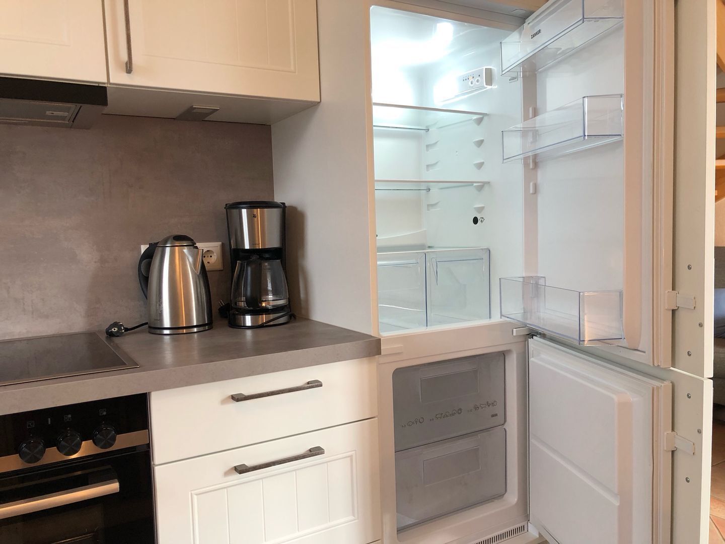 A modern kitchen with a built-in refrigerator, a coffee maker, and a kettle on the countertop.