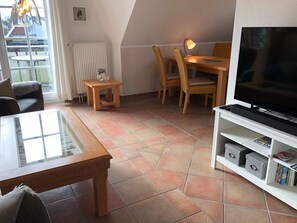 A living room with a TV, a dining table, chairs, a coffee table, and a bookshelf.