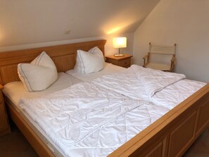 A neatly made bed with white bedding and pillows, a wooden headboard, a bedside lamp, and a wooden nightstand.